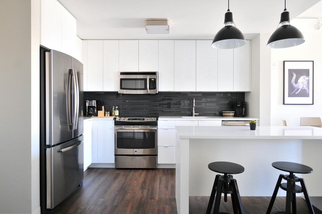 White kitchen with a stainless-steel fridge and range, two black pendant lamps and two stools at the island
