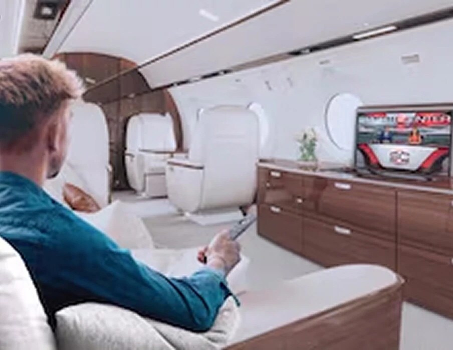 Seen from behind, a man in a teal shirt points a remote at a cabinet TV inside an aircraft cabin