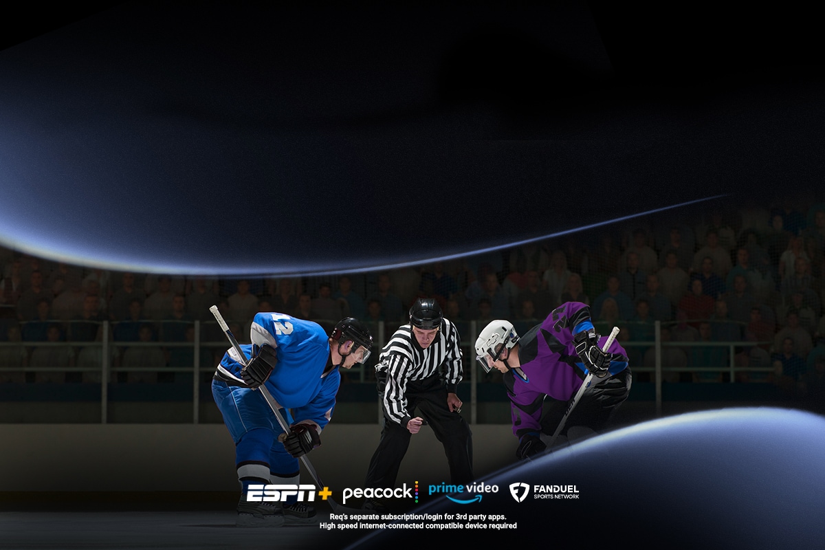 Hockey players in blue and purple jerseys crouched for a faceoff as a referee looks on