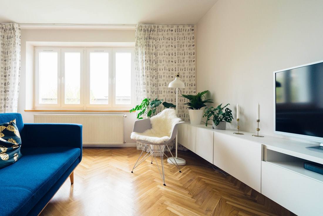 A bright living room with a blue sofa, a white chair and a TV on a low cabinet