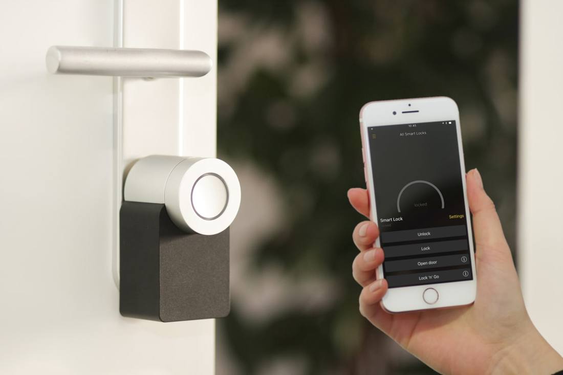 A hand holding a phone with a smart-lock app beside a lock on a white door