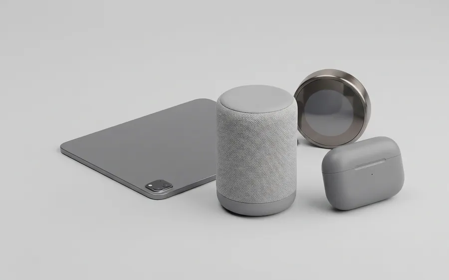 A tablet, a fabric-covered smart speaker, an earbuds case and a round thermostat on a gray surface