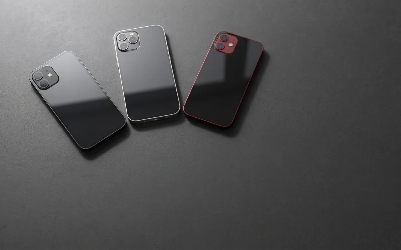Three smartphones lying face down on dark gray stone, one with a red frame