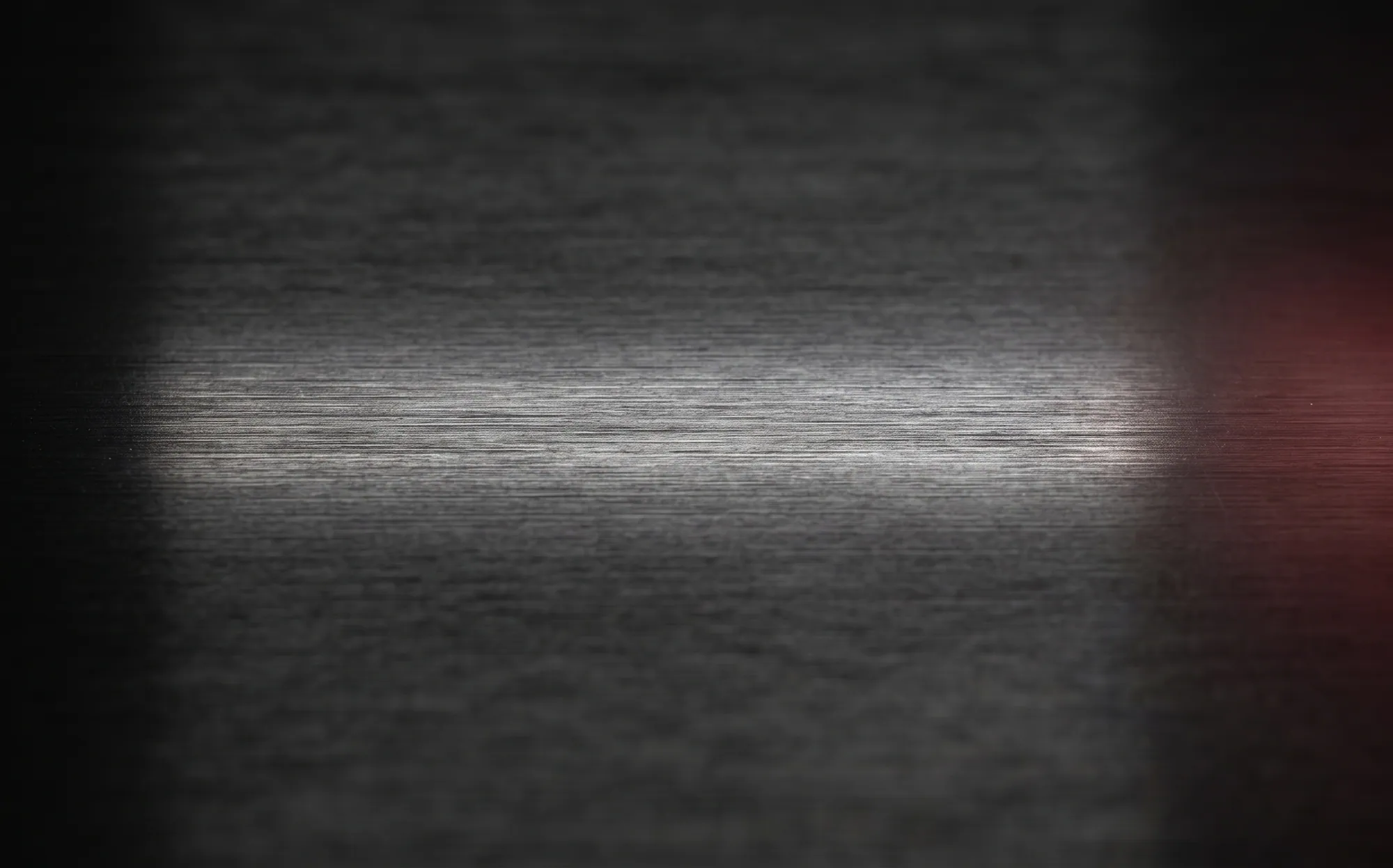 Dark brushed metal lit by a horizontal band of light, with a red glow at the right edge